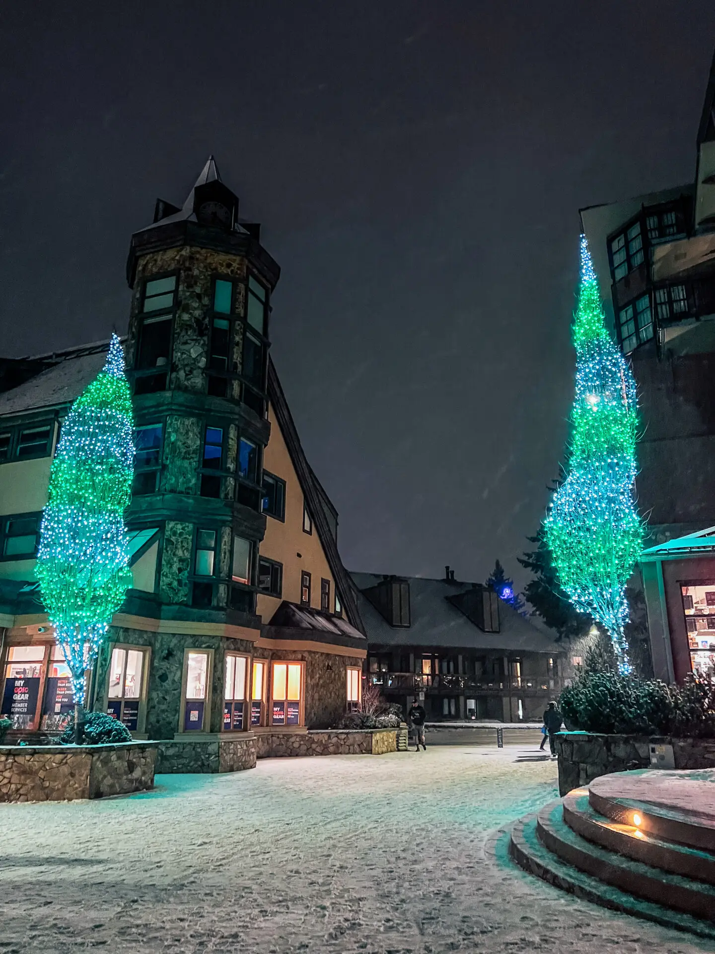 Snowfall over the main street of Whistler Village with alpine shops and skiers walking through town.